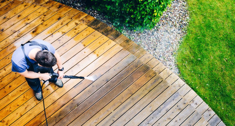 man cleaning terrace with a power washer - high water pressure cleaner on wooden terrace surface